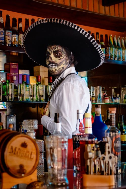 Free A bartender with Day of the Dead face paint and traditional attire at a lively bar setting. Stock Photo