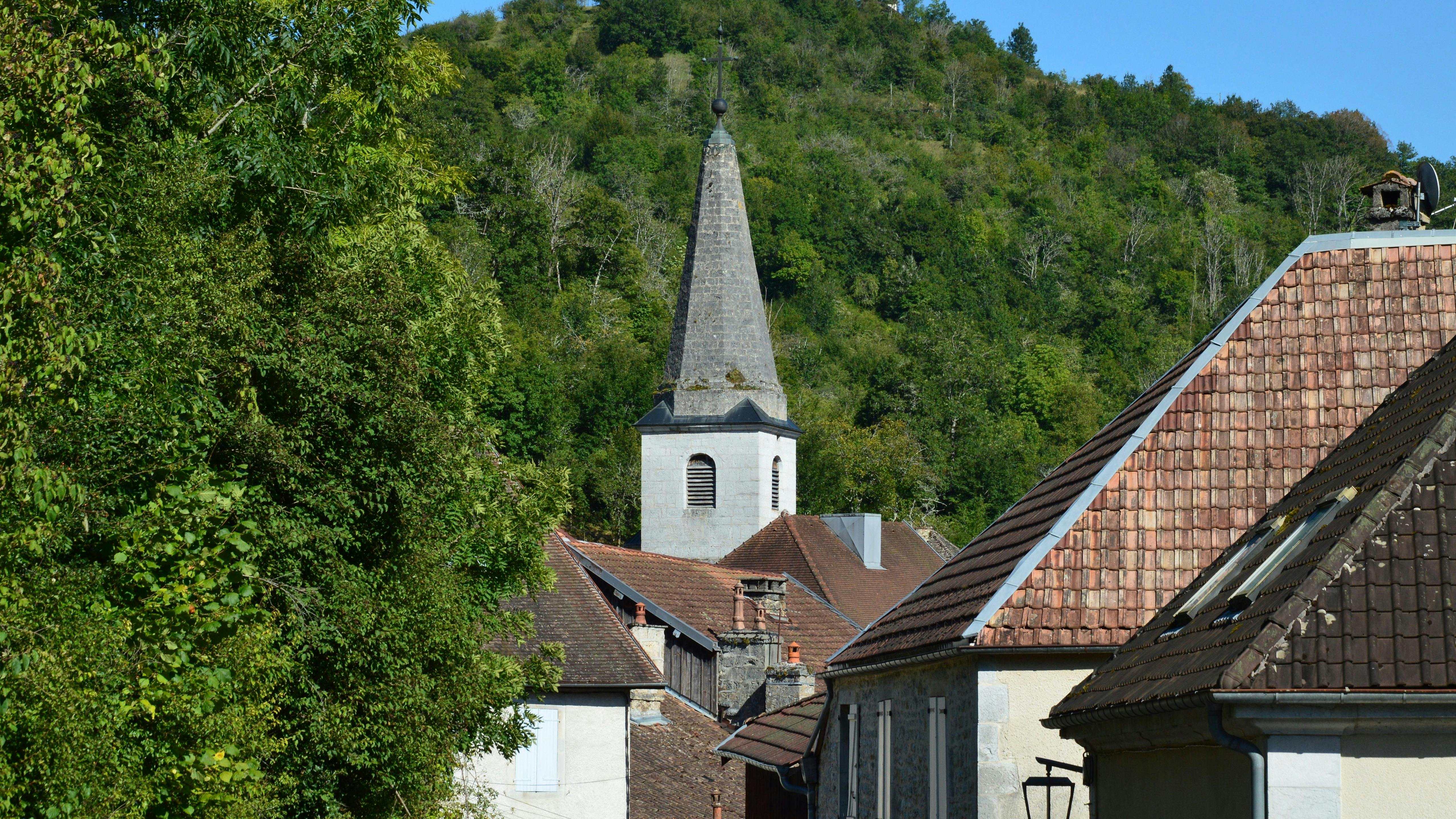 Quaint church steeple amidst rustic rooftops and lush greenery in Lods, France, capturing serene rural charm.