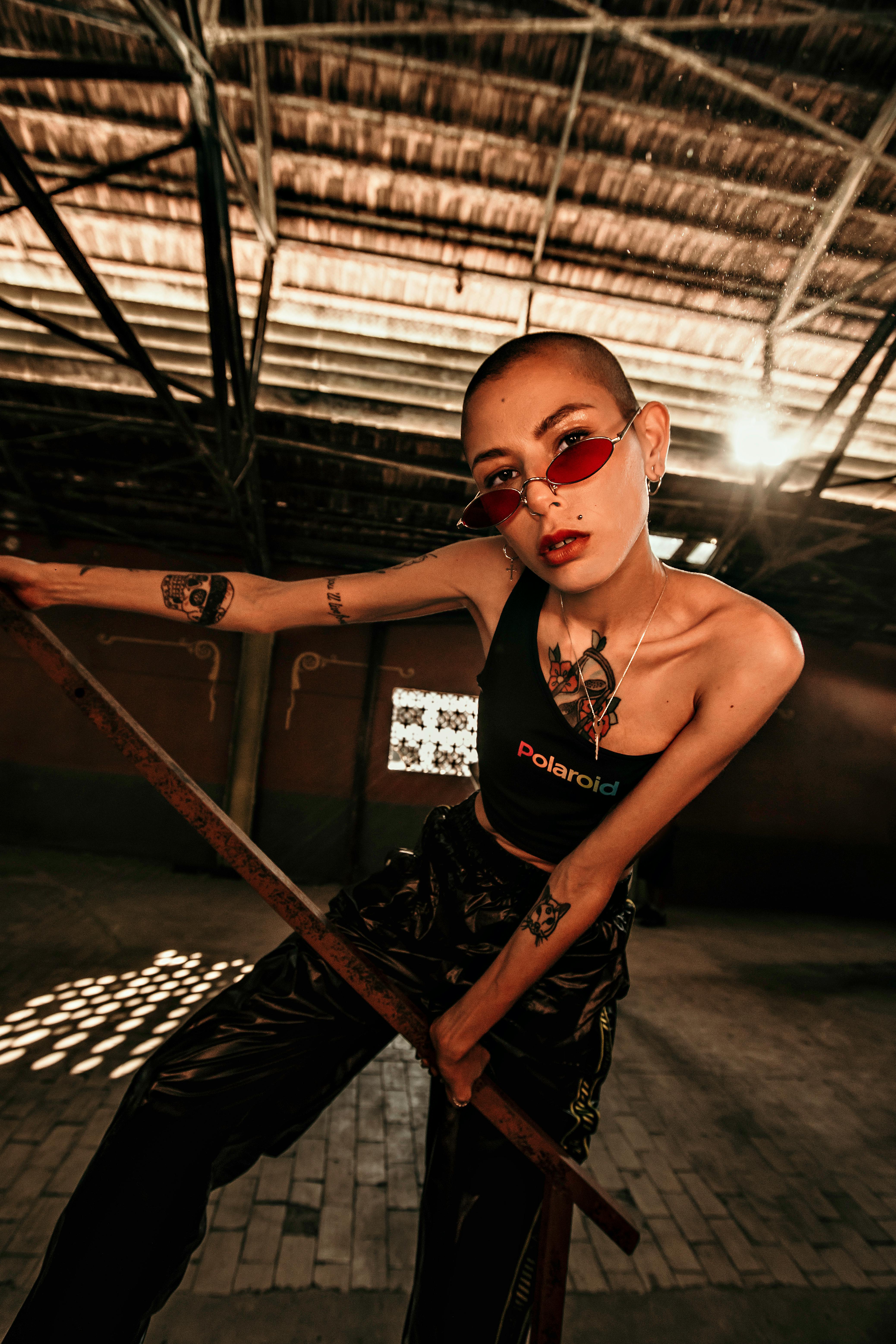 一位时尚的纹身女子戴着太阳镜，穿着休闲服，在室内自信地摆着姿势