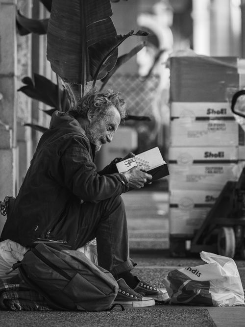 Free Black and white image of a man reading on a city street, evoking thoughtfulness. Stock Photo