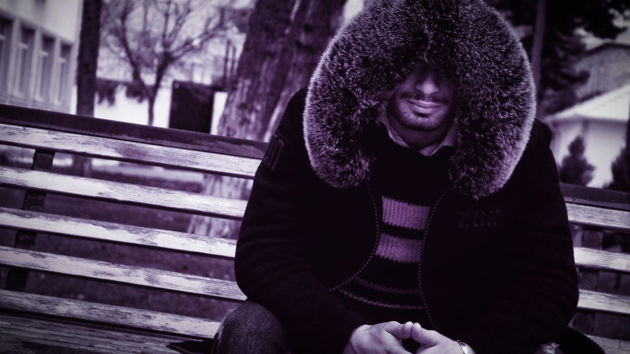 a mysterious man in a fur hooded coat sits on a park bench exuding a c