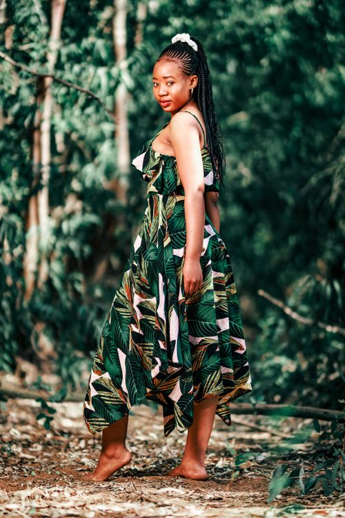 Free A woman poses barefoot in a stylish dress amidst a lush forest backdrop. Stock Photo