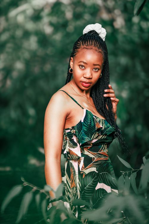 Free A woman with braided hair poses confidently in a lush forest while wearing a colorful, tropical dress. Stock Photo
