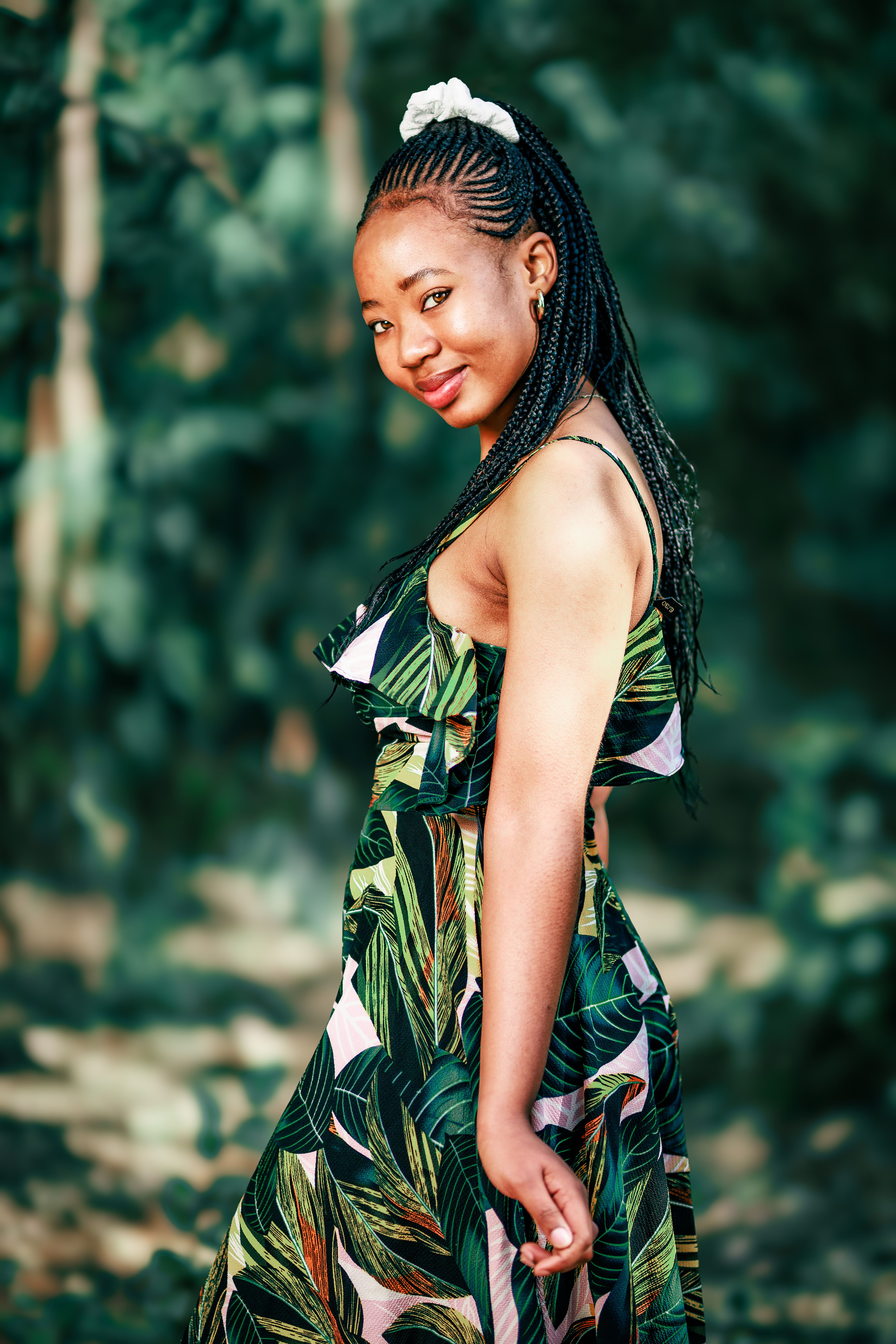 A woman in a stylish leafy dress poses outdoors with a confident smile.
