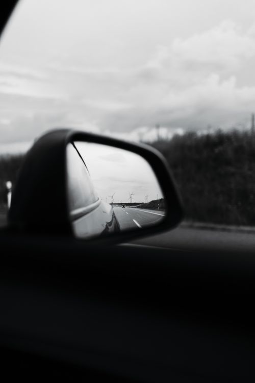 Free A black and white photo capturing a road reflected in a car mirror on a cloudy day. Stock Photo