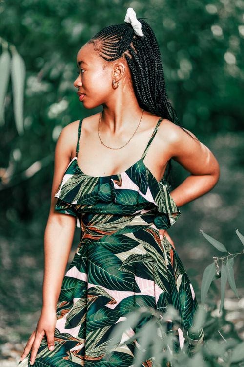 Free Young woman with braided hair in a patterned dress posing in a lush green forest. Stock Photo