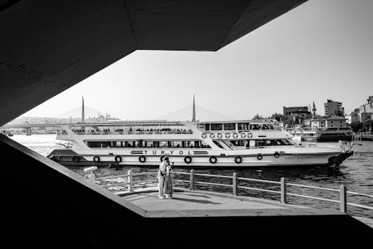 Black and white photo of a ferry near an Istanbul bridge, capturing urban life.