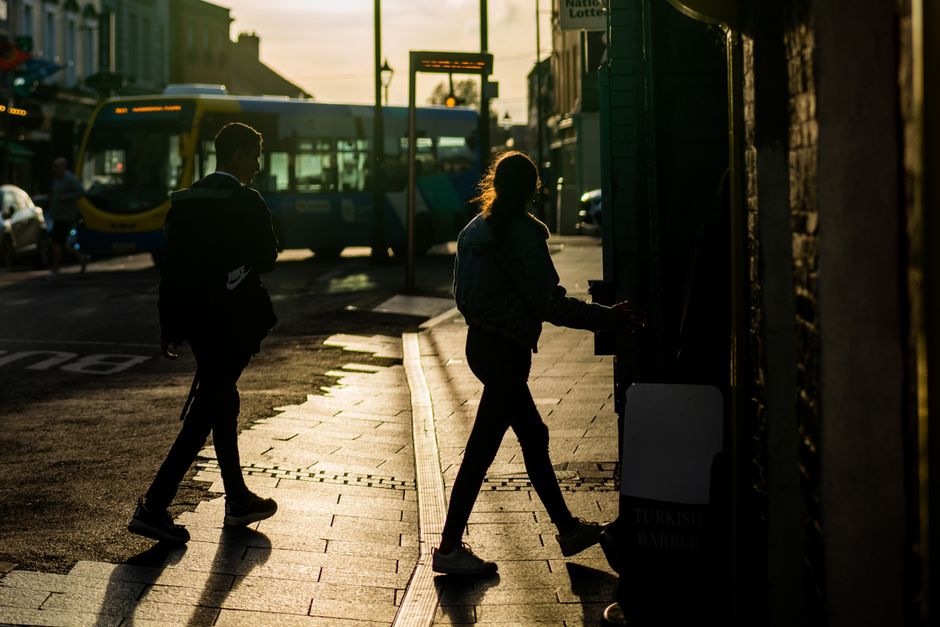 Silhouetted figures walk on a busy street in Navan against a sunset backdrop, capturing urban life.