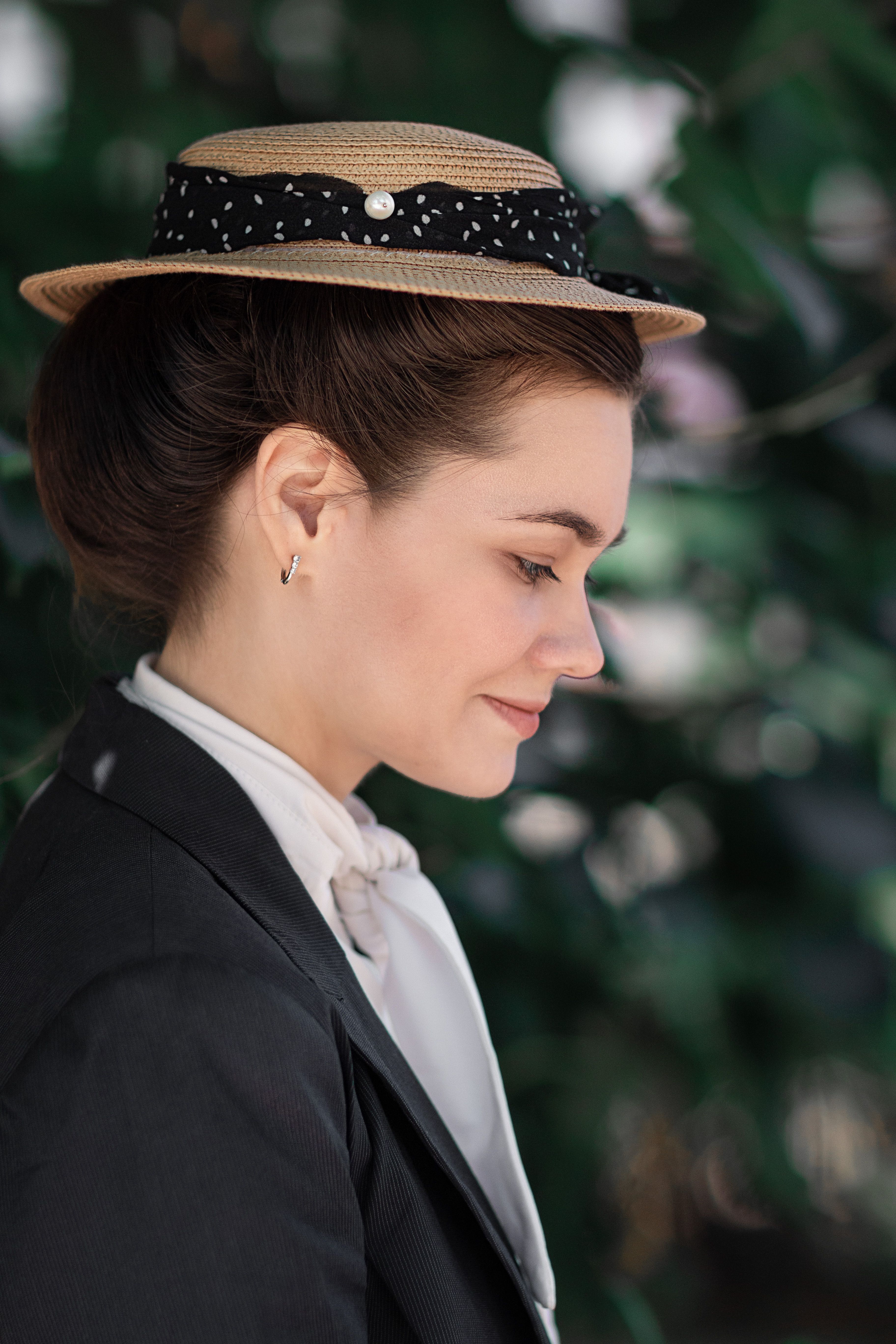 Profile portrait of a woman in vintage attire with a straw hat outdoors.