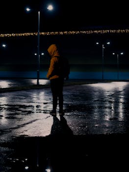 A man in silhouette stands on a wet street under streetlights in Bratislava, creating a moody night scene.