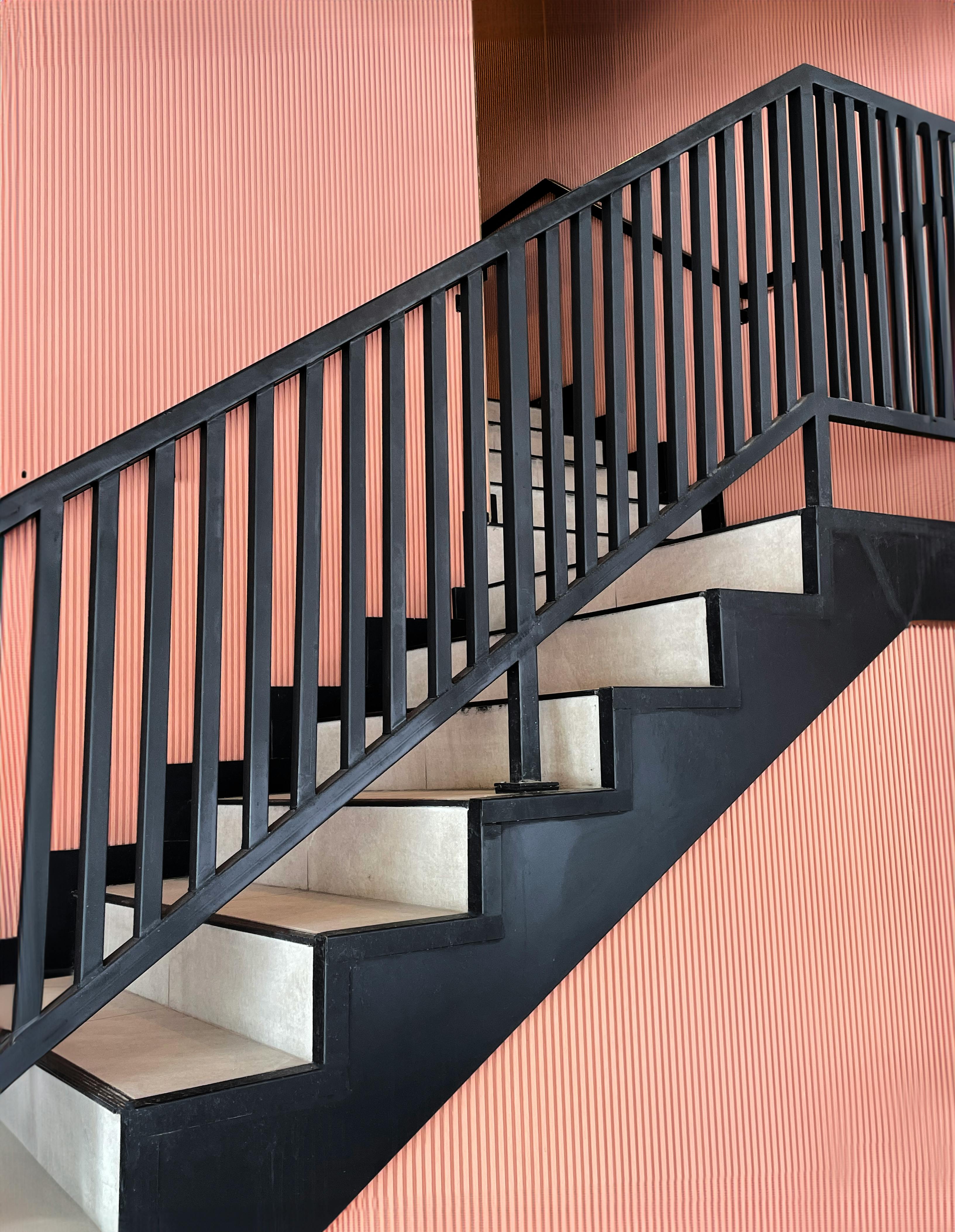 a black railing with white steps and a pink wall