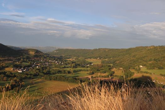 Beautiful countryside landscape at sunset featuring rolling hills, green fields, and a small village.