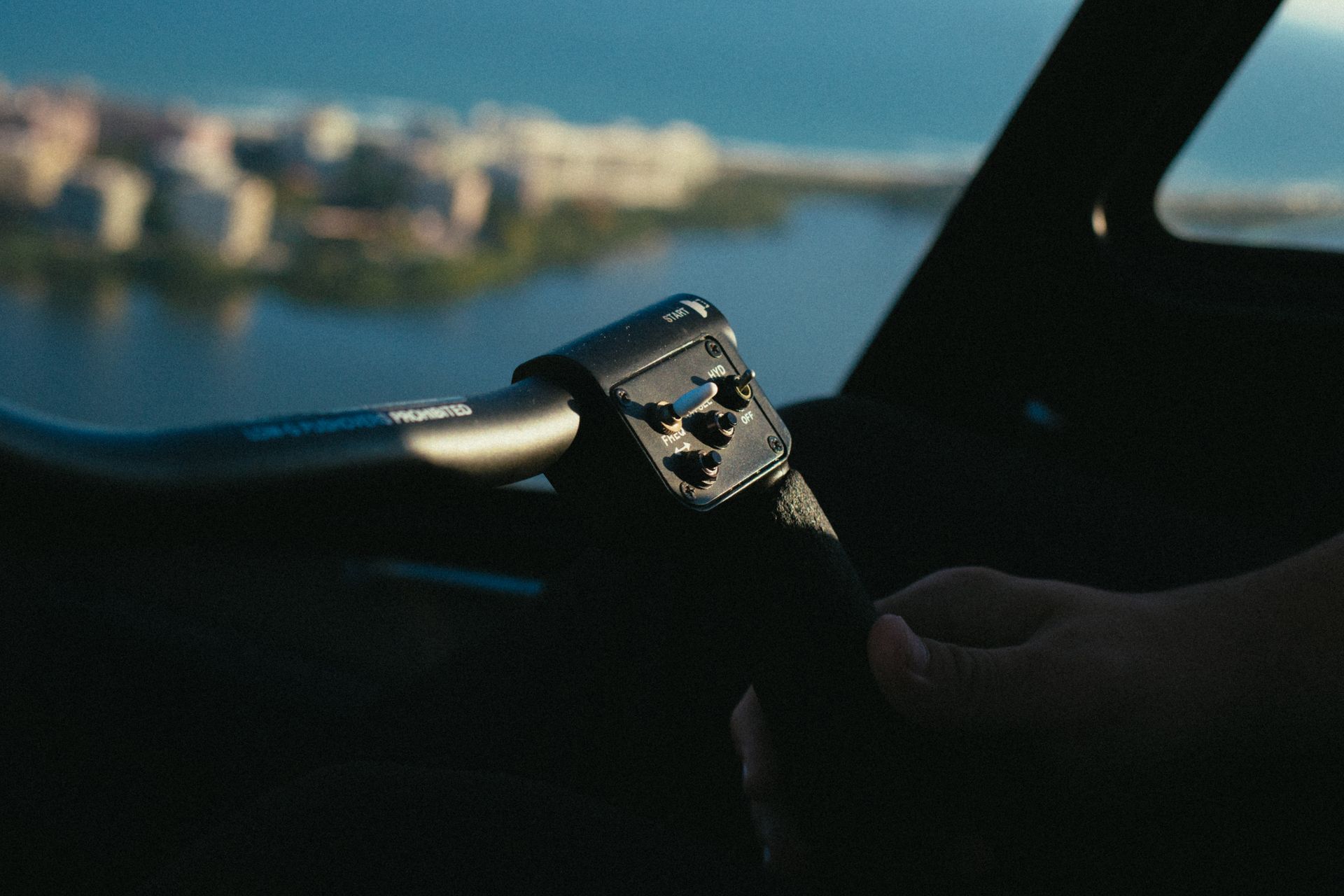 A person's hand gripping an aircraft control inside a cockpit during daytime.