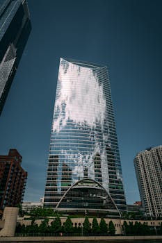 城市中，高层建筑的玻璃立面映照着云彩，象征着现代建筑