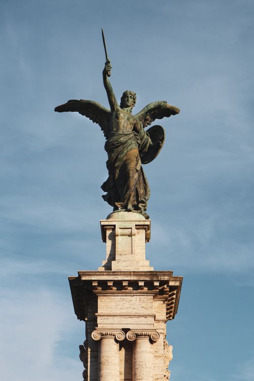 Free Majestic angel statue atop a classical column against a clear blue sky in Rome, Italy. Stock Photo