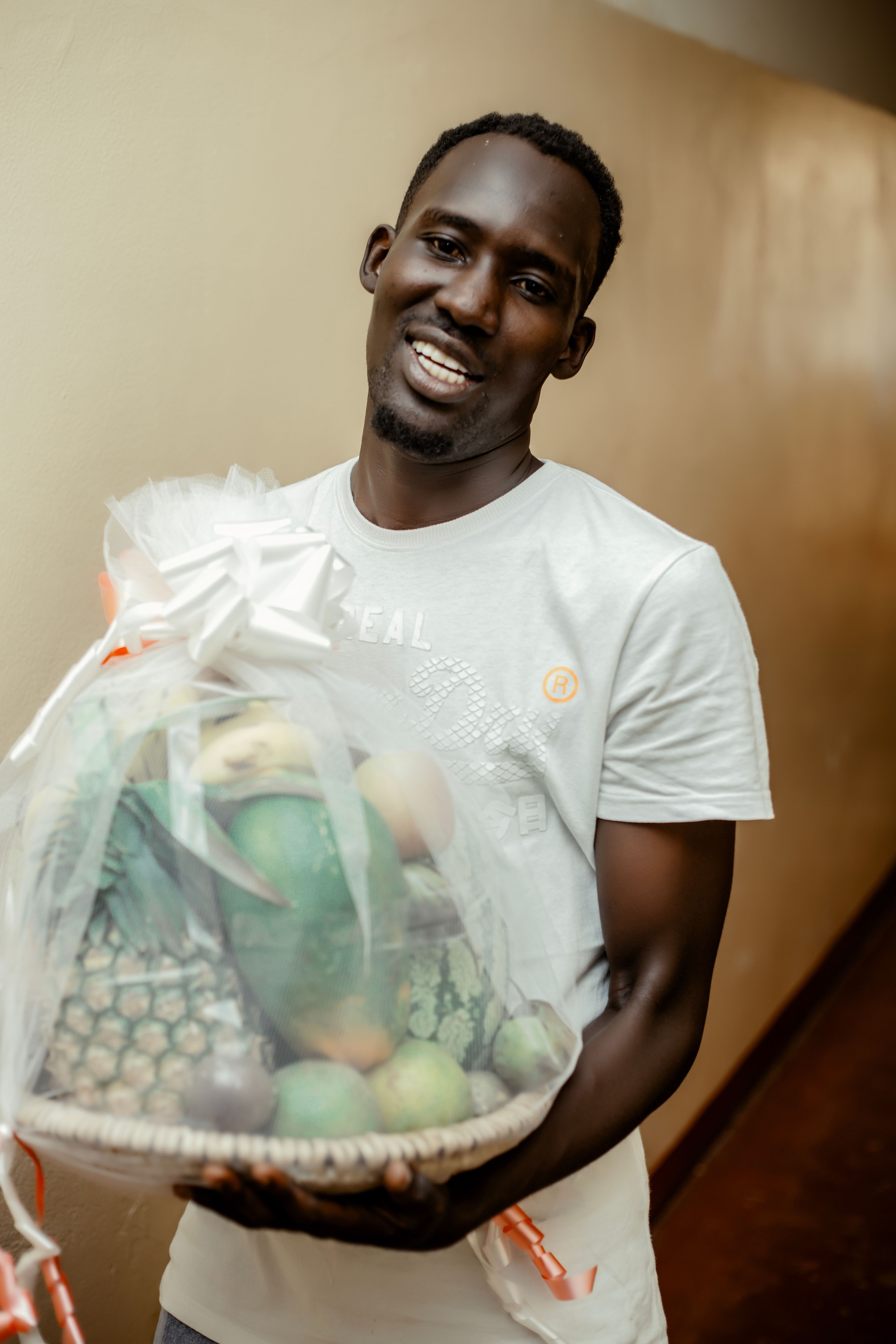 Young man with a fruit basket smiling warmly indoors.