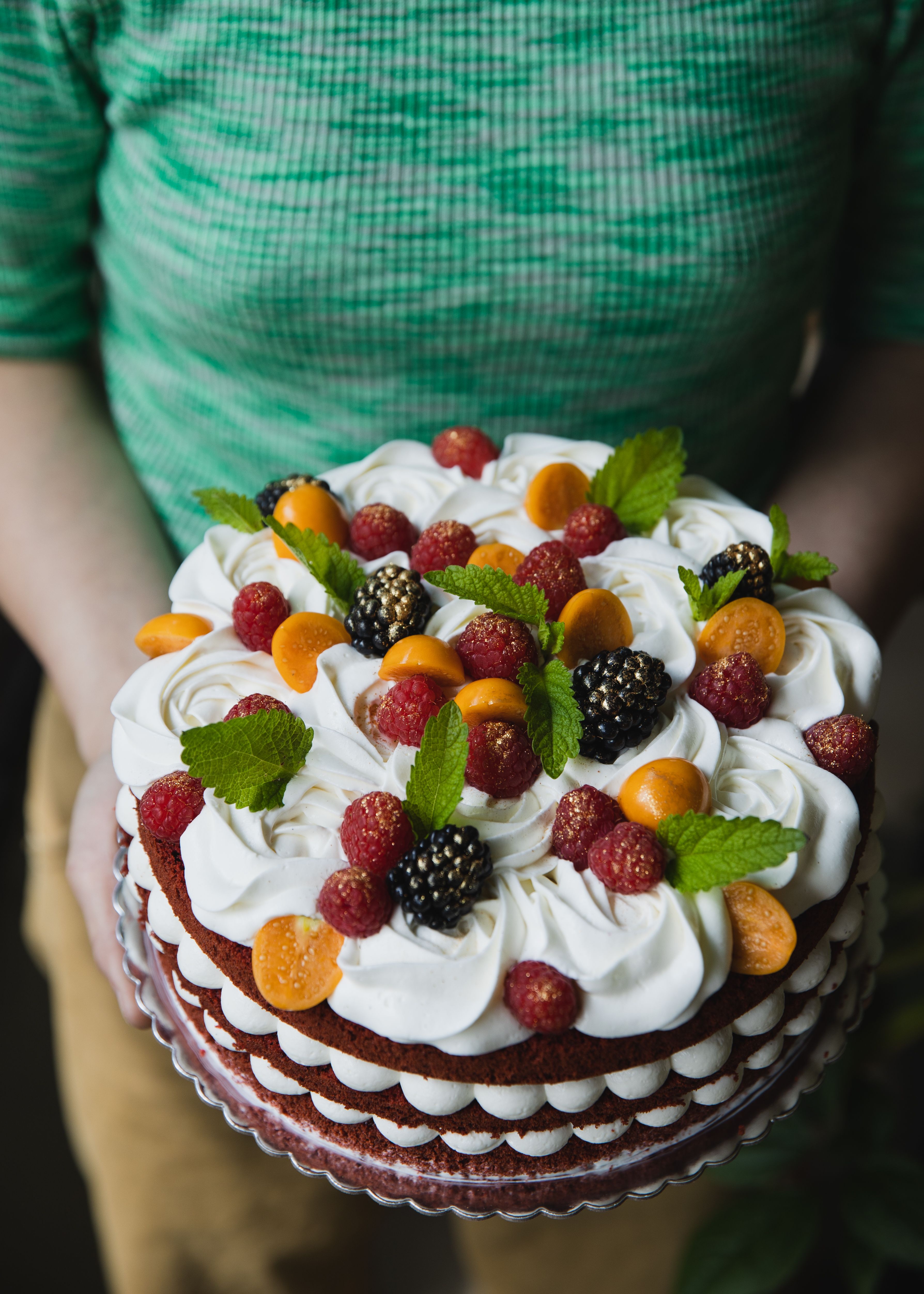 A beautifully decorated cake topped with fresh berries, mint, and cream, perfect for dessert presentations.