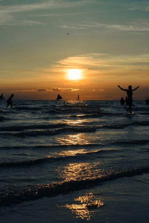 Free A stunning beach sunset in Manila with silhouettes and shimmering waves. Stock Photo