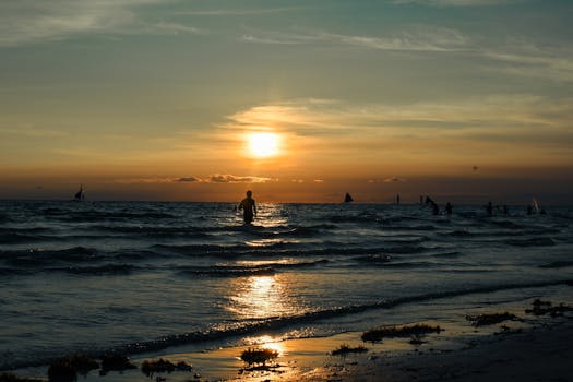 Silhouetted figure at sunset with sailboats and gentle waves in Kalibo, Philippines.