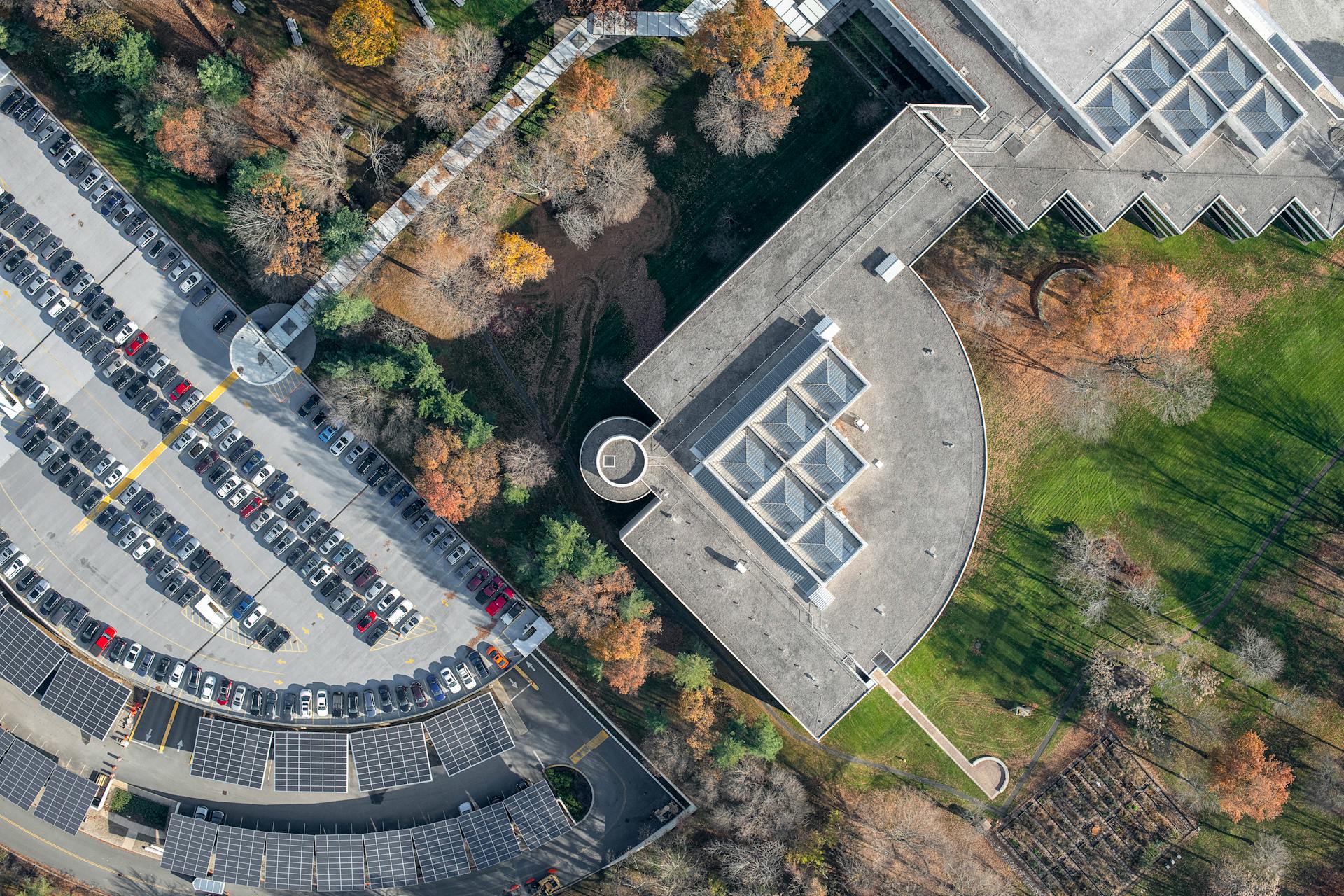 Aerial photo capturing the structure of a modern building next to a busy parking lot surrounded by autumn trees.