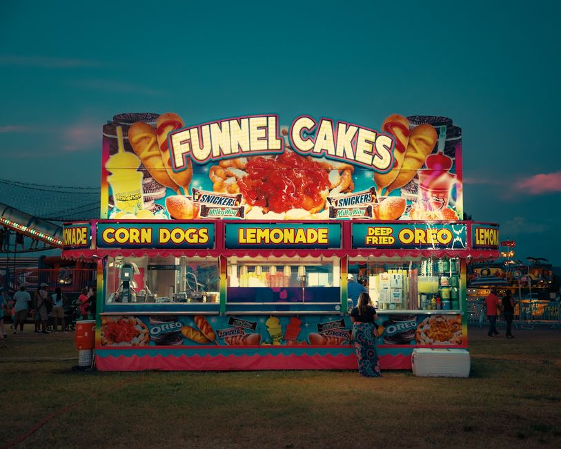 Colorful funnel cake stand illuminating a bustling carnival evening.