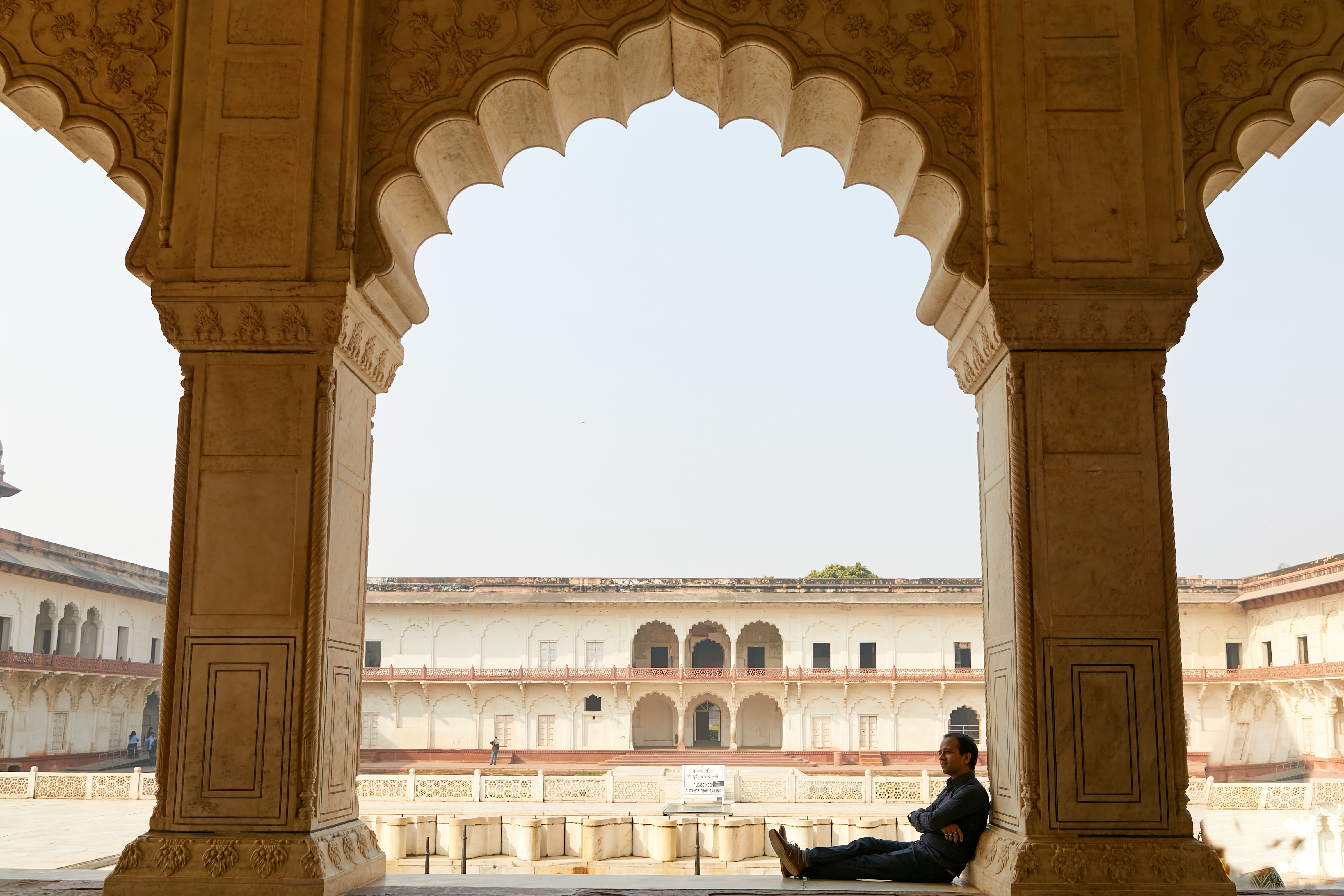A man relaxes under the arched corridor of Agra Fort, India, showcasing Mughal architecture. - Agra