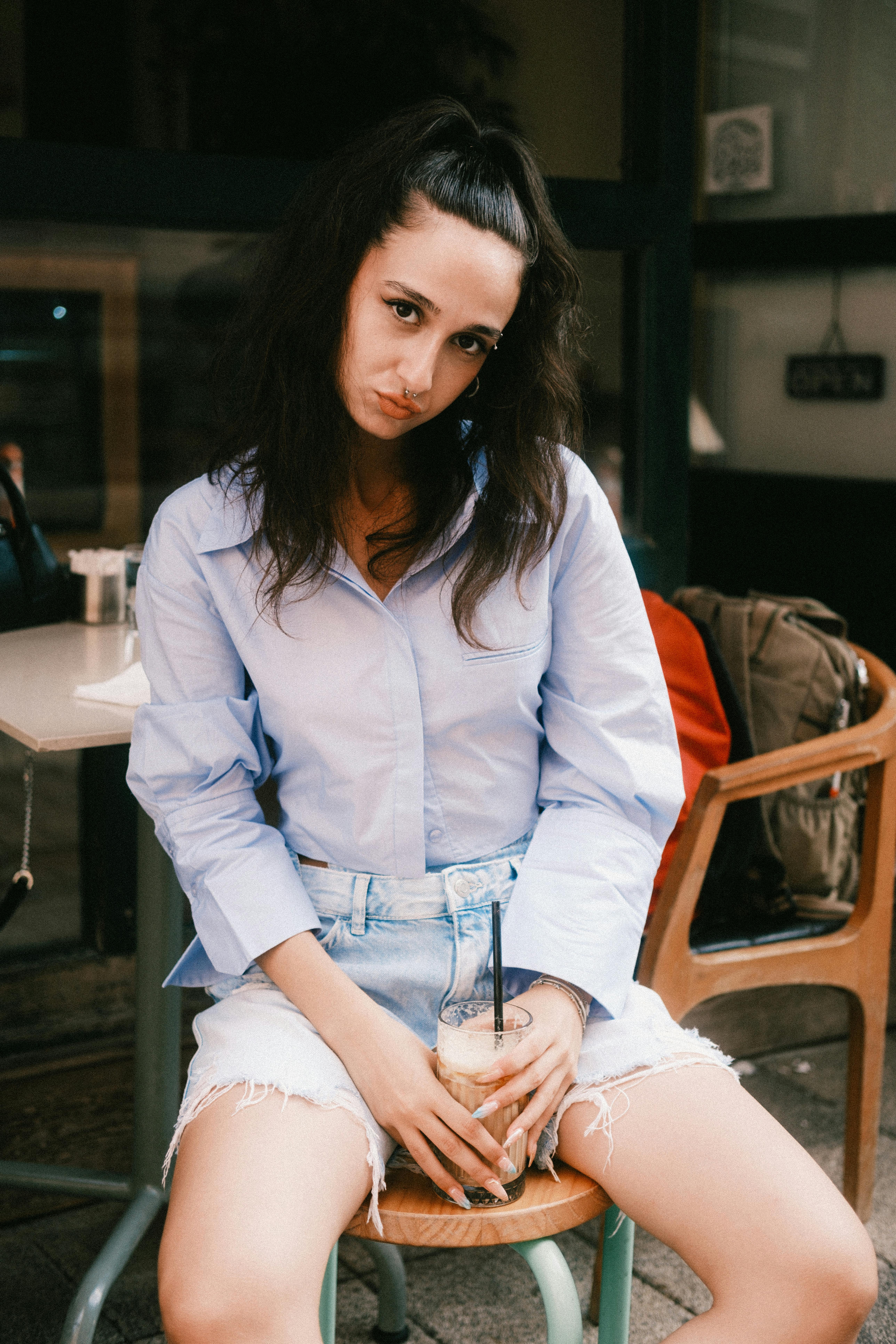 Relaxed woman in casual attire enjoying a drink indoors on a chair.