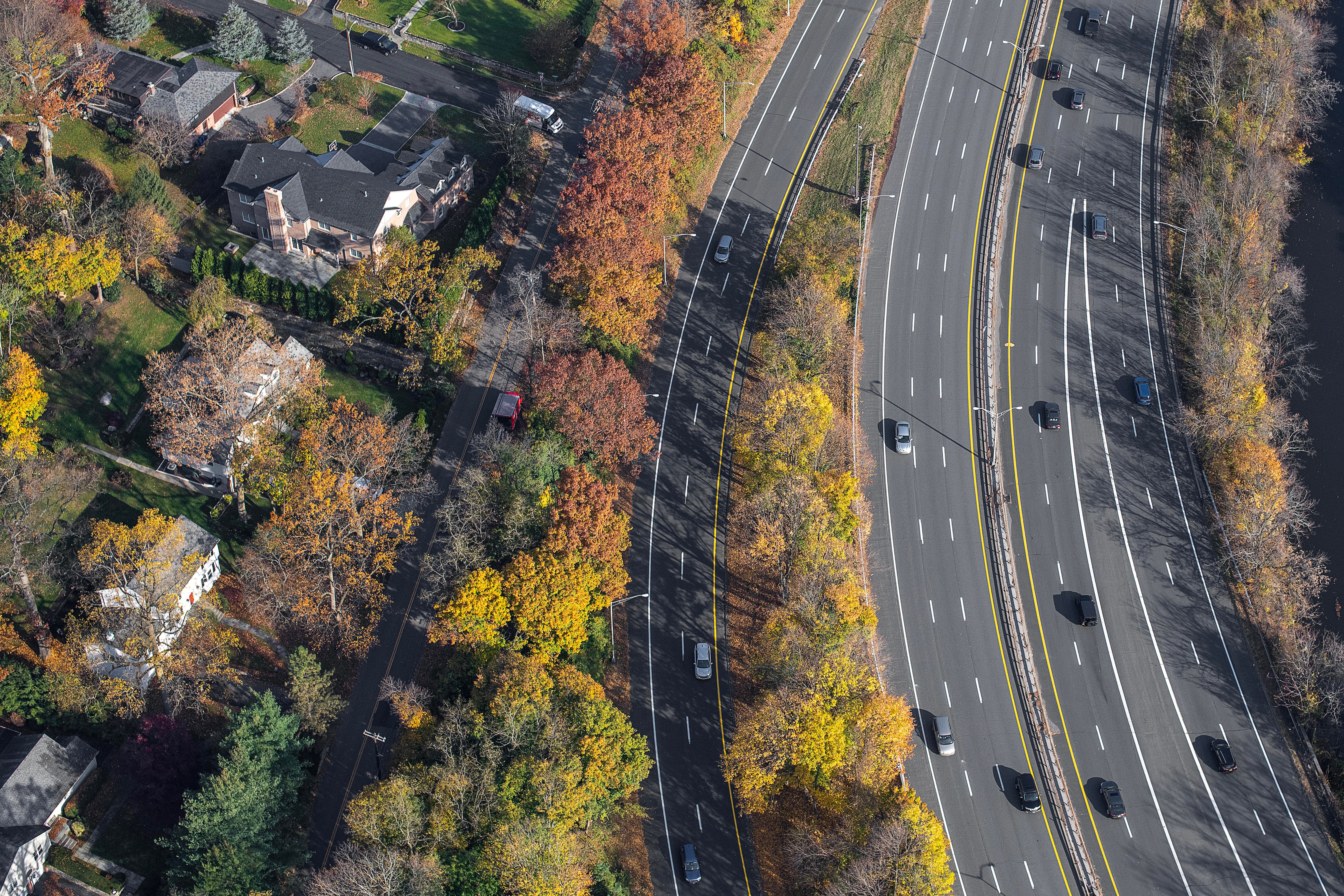 Aerial view depicting a highway with traffic amidst vibrant autumn trees and nearby residential area.