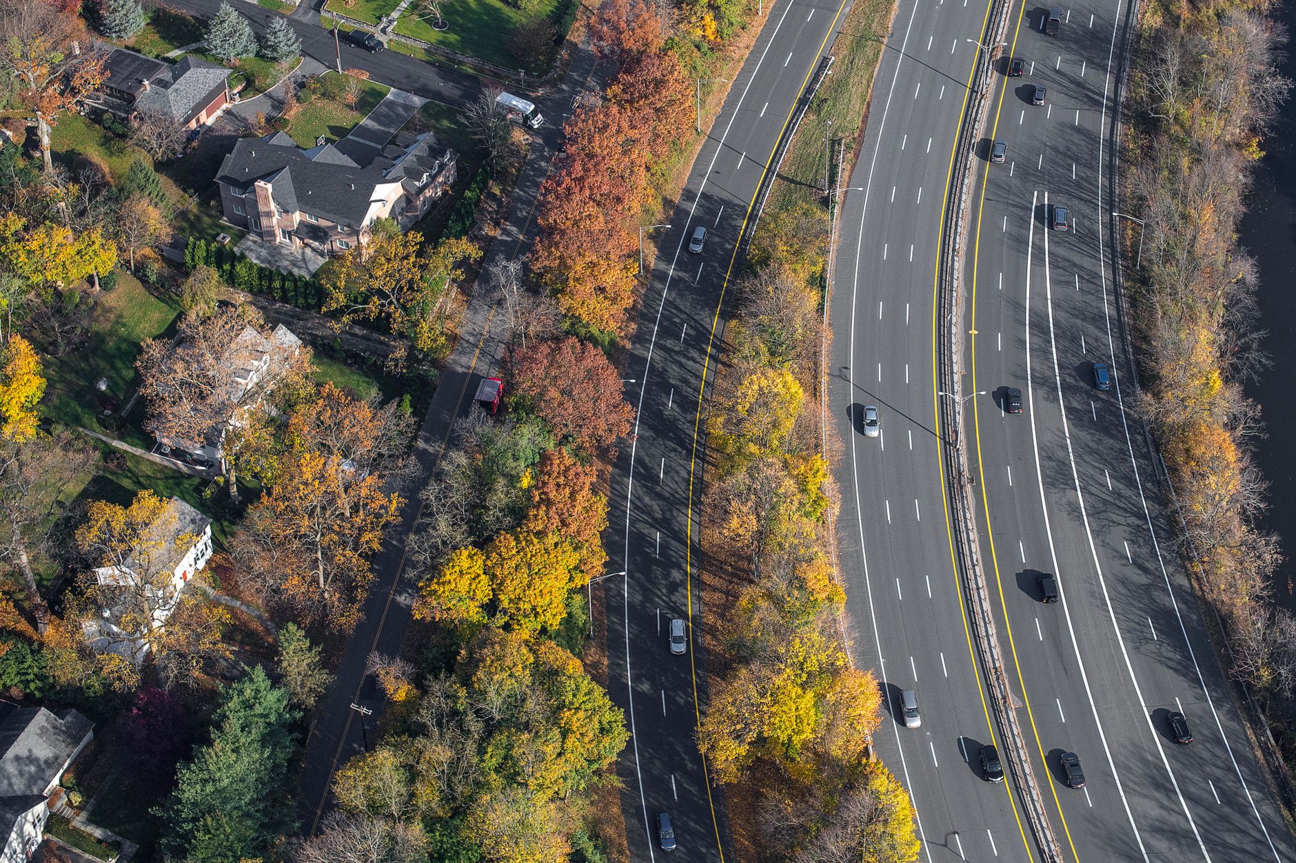 Aerial view depicting a highway with traffic amidst vibrant autumn trees and nearby residential area.