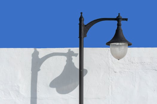 A vintage street lamp casting a shadow on a white wall under a clear blue sky.