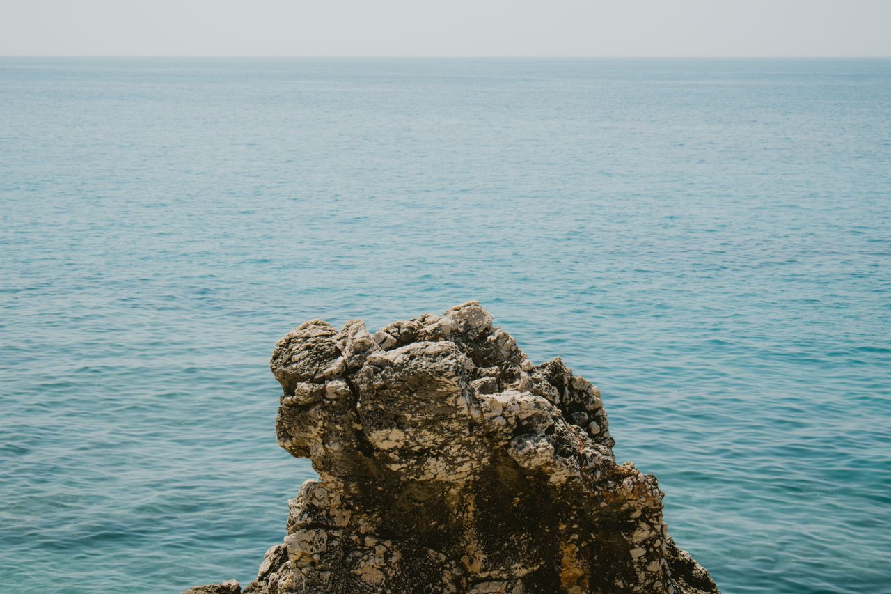 a tranquil seascape with a rocky outcrop against the blue ocean in vlo