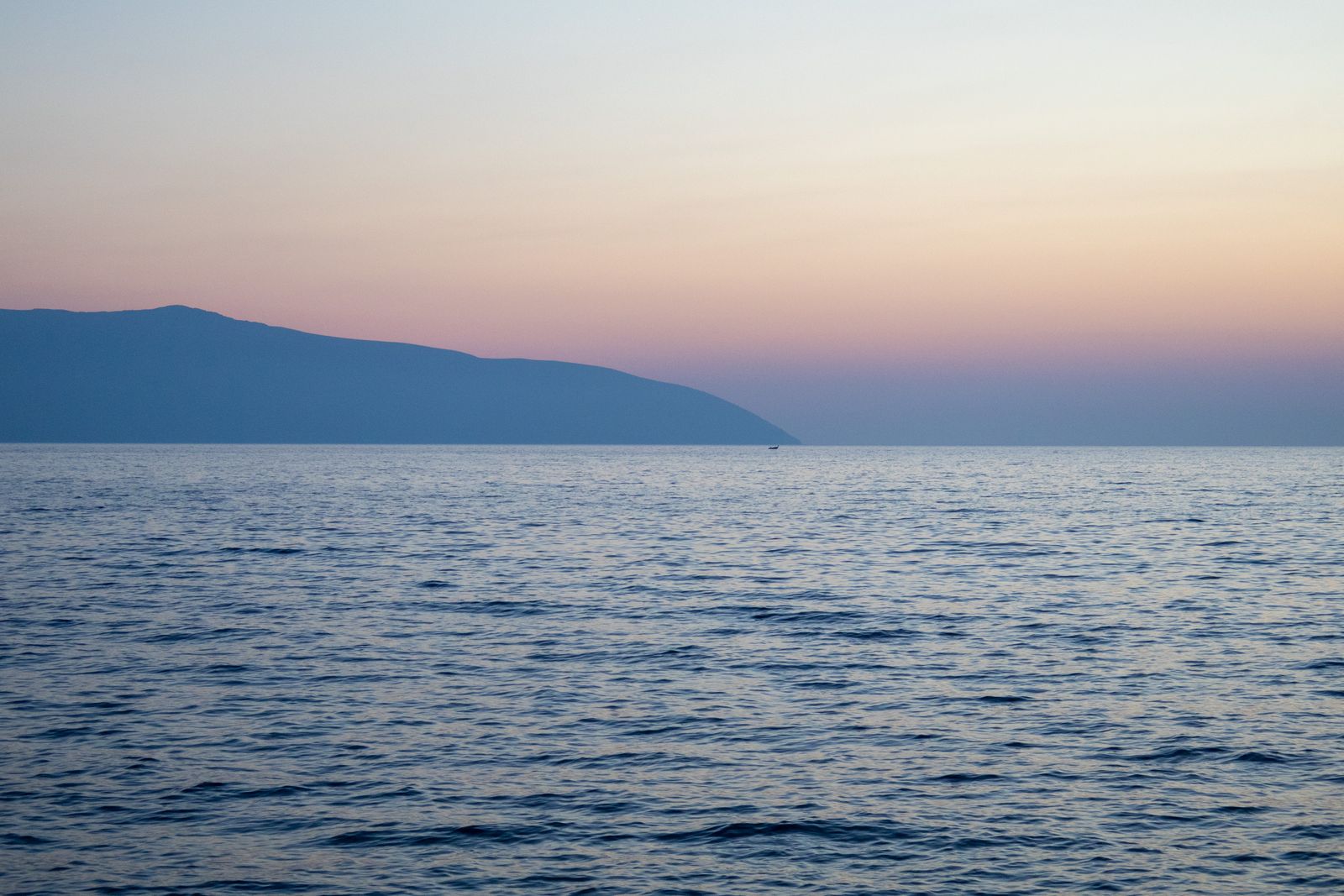Serene sunset view of Vlora coast with calm sea and distant hills under a pastel sky.