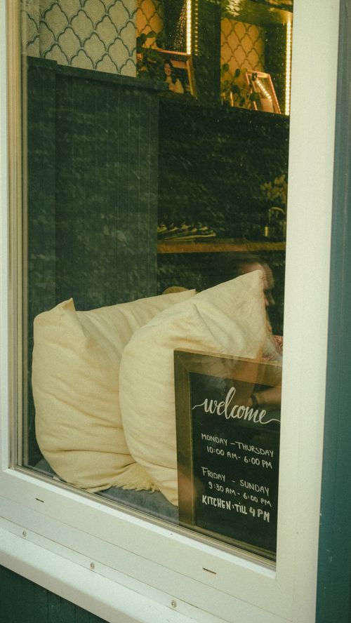 Free View through window of cozy cafe interior with pillows and welcome sign. Stock Photo