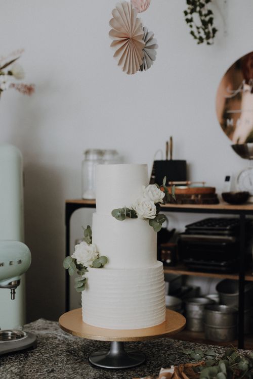 Free Minimalist white wedding cake adorned with flowers in a stylish kitchen setting. Stock Photo