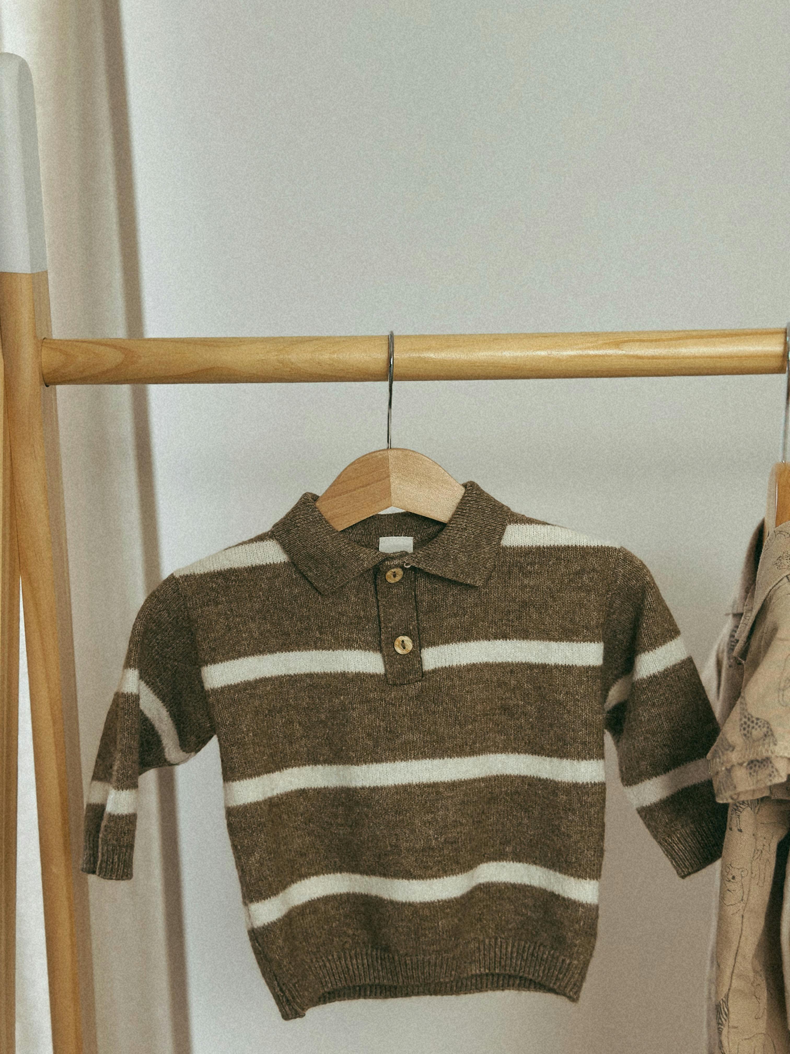 Brown and white striped children's sweater hanging indoors, minimalist style.