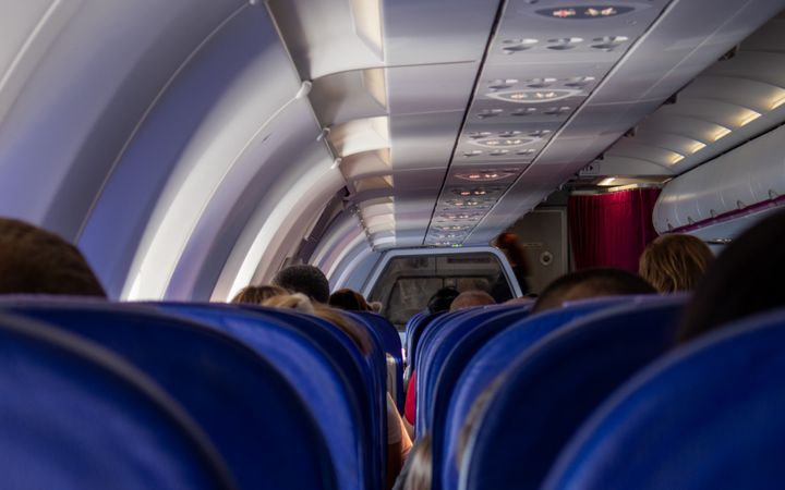 Rows of blue airplane seats and passengers inside an aircraft during flight, showcasing travel and transportation.