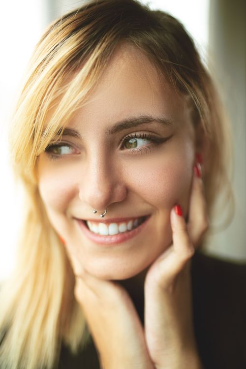 Free Close-up of a blonde woman smiling joyfully, highlighting her nose piercing. Stock Photo
