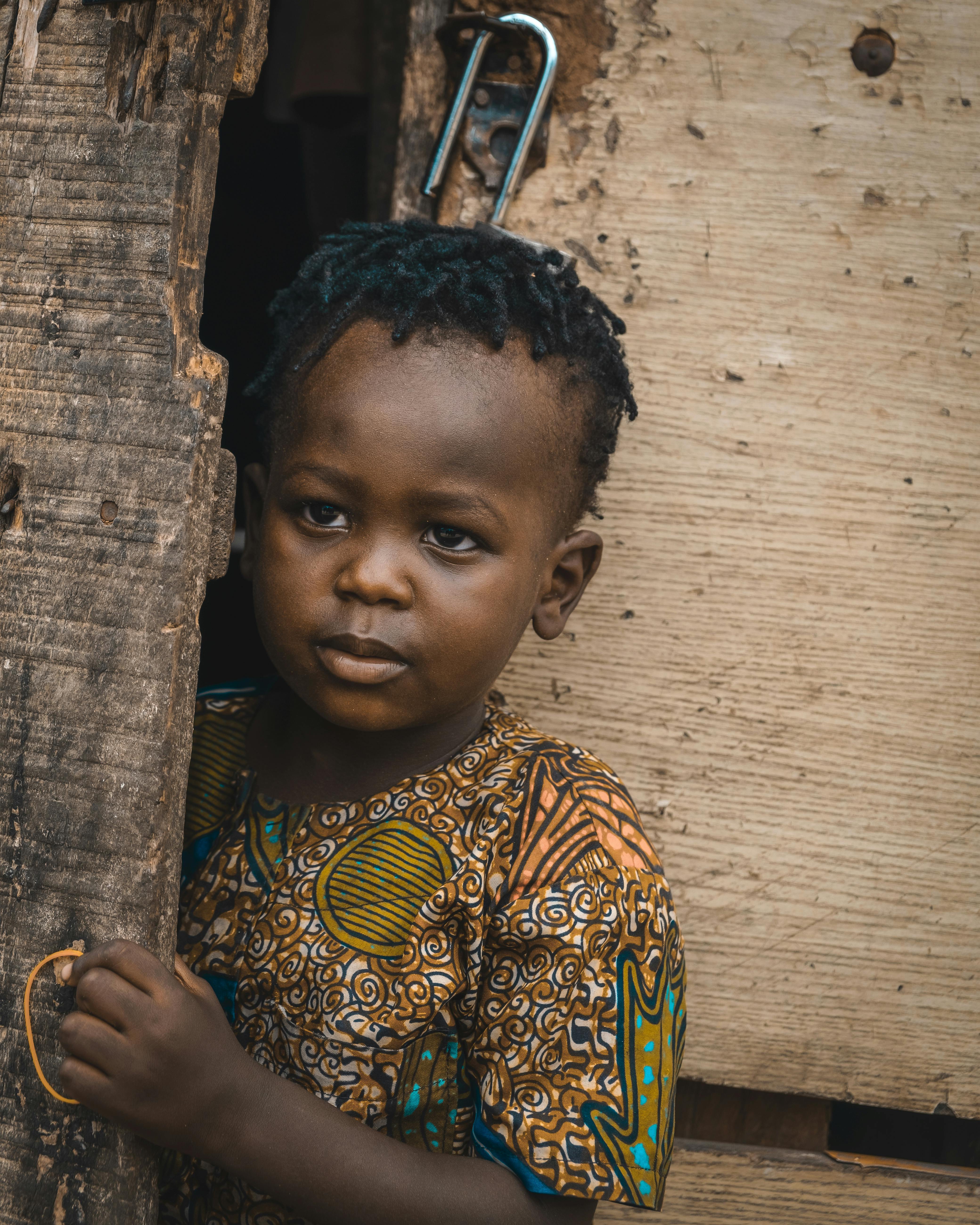 a young african child looking out of a wooden door