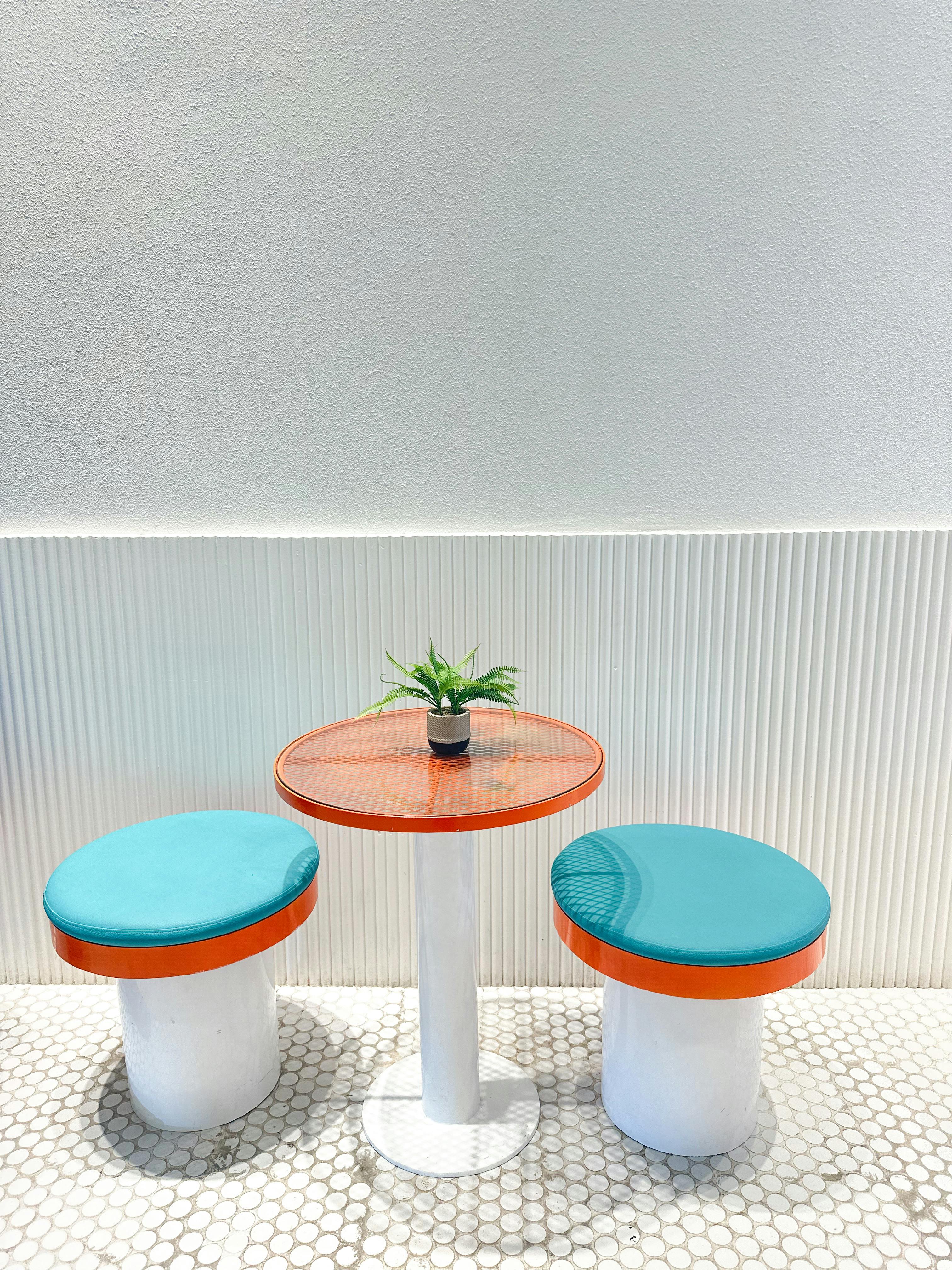 two stools with blue and orange seats and a plant