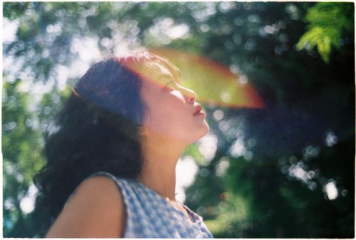 Free Serene portrait of a woman enjoying sunlight in a lush green park, captured with bokeh effect. Stock Photo