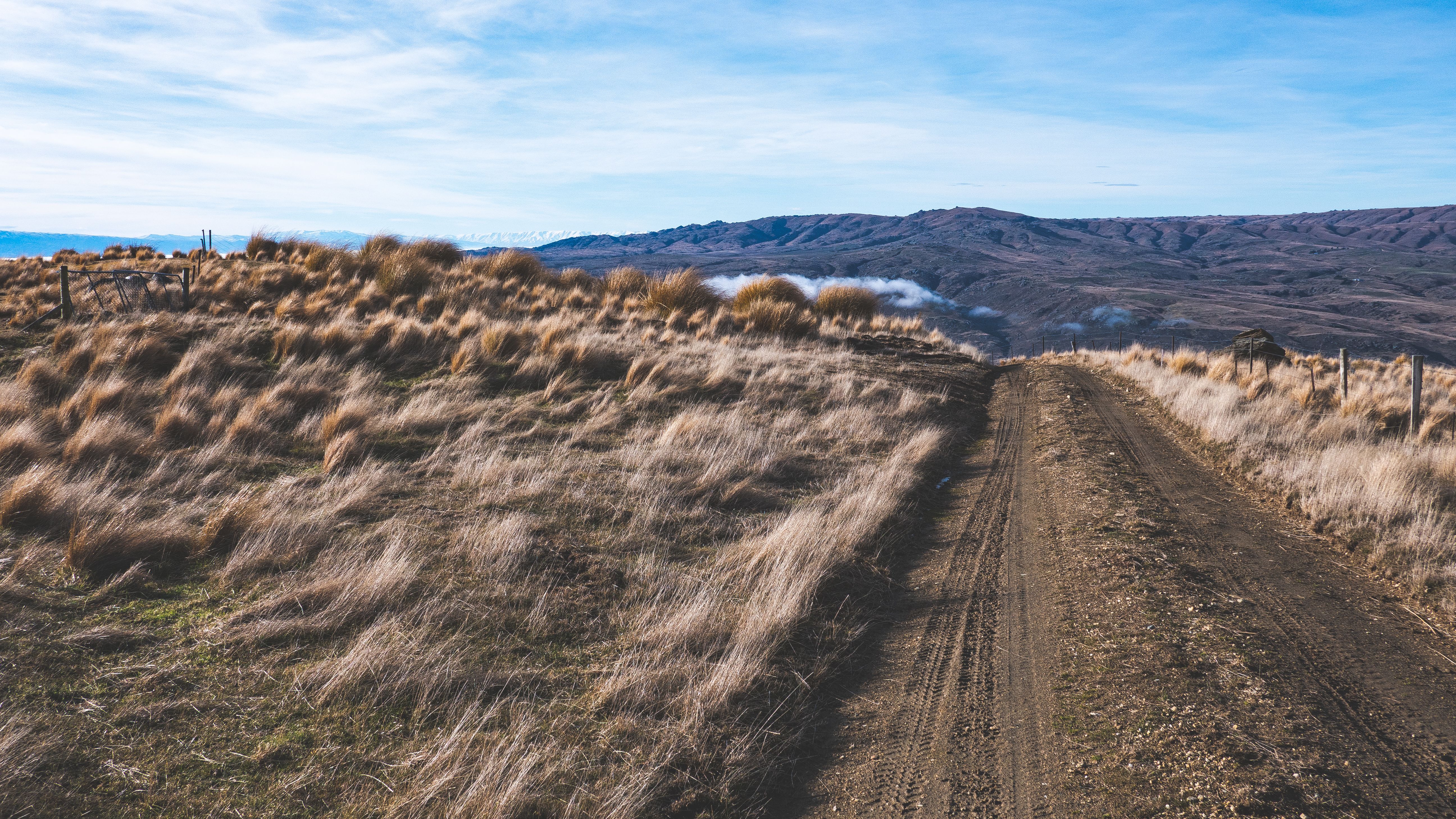 A dirt road with grass and mountains in the background · Free Stock Photo