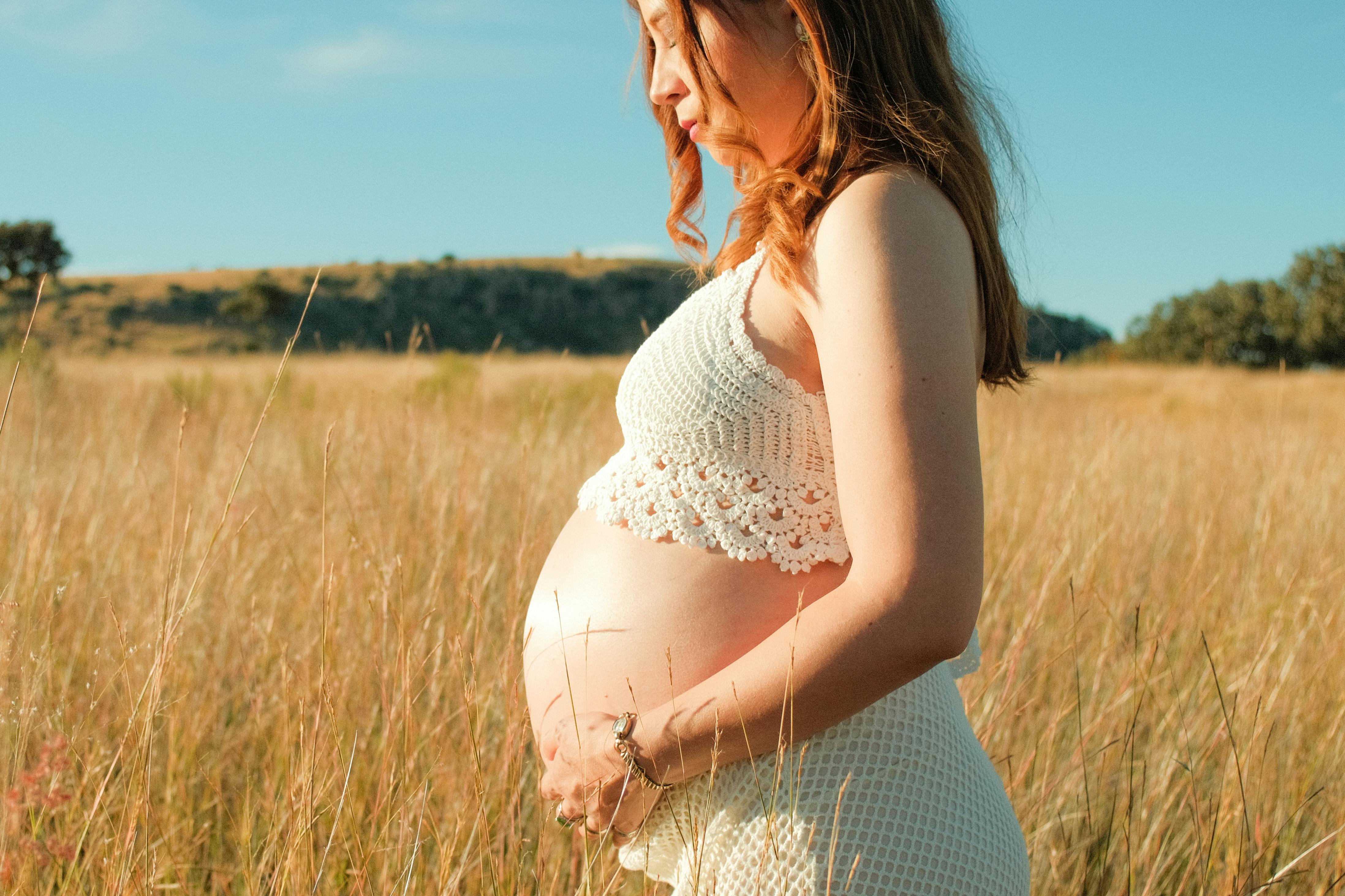 a pregnant woman in a field with a long dress