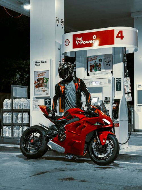 Free Rider beside red Ducati motorbike refueling at Shell station at night. Stock Photo