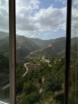 View of Dagestan mountains from Sogratl window with winding roads and lush greenery.