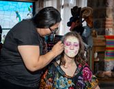An artist paints traditional Catrina makeup on a woman during a cultural festival in Mexico City.