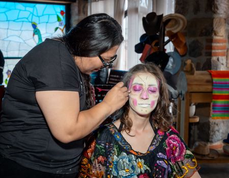 An artist paints traditional Catrina makeup on a woman during a cultural festival in Mexico City.