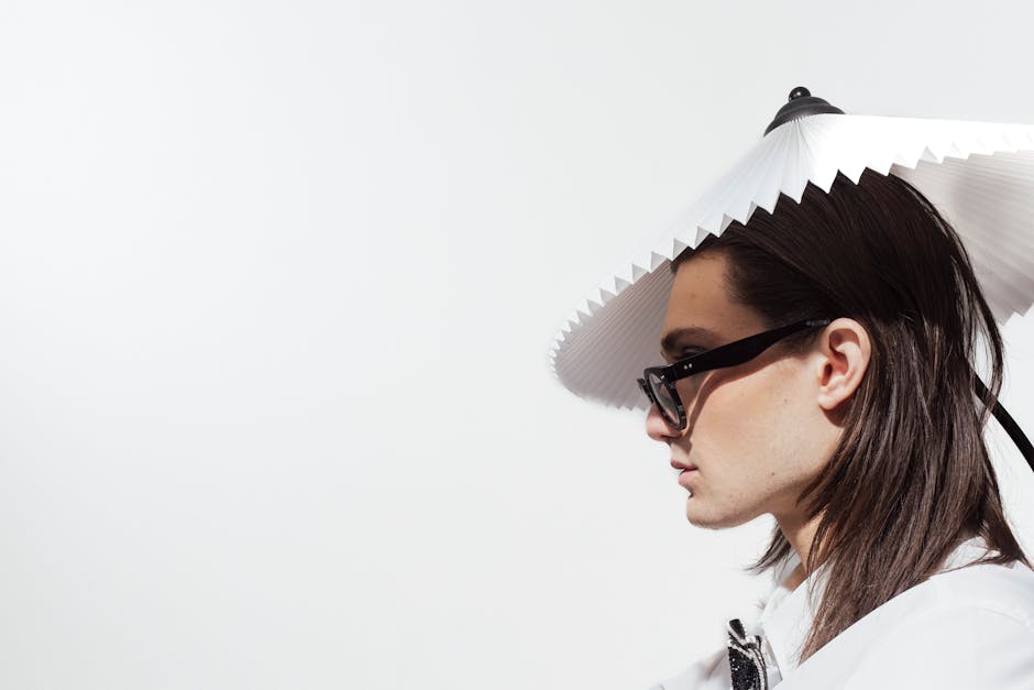 Profile portrait of a man wearing eyeglasses and a unique lampshade hat against a white background.