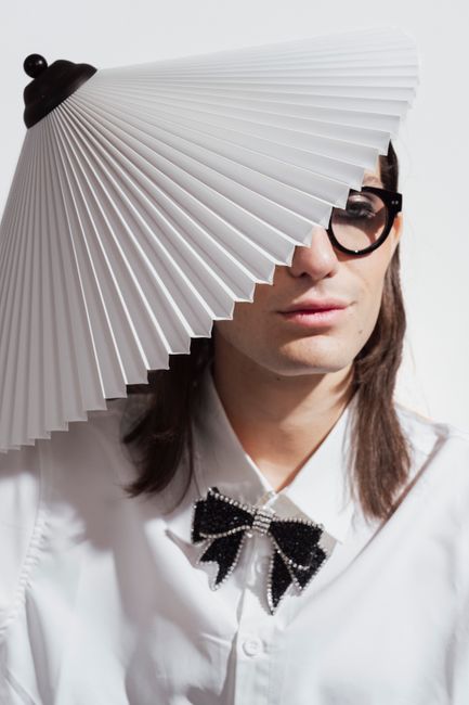 A stylish person in glasses with creative fashion sense, wearing a lampshade hat indoors.