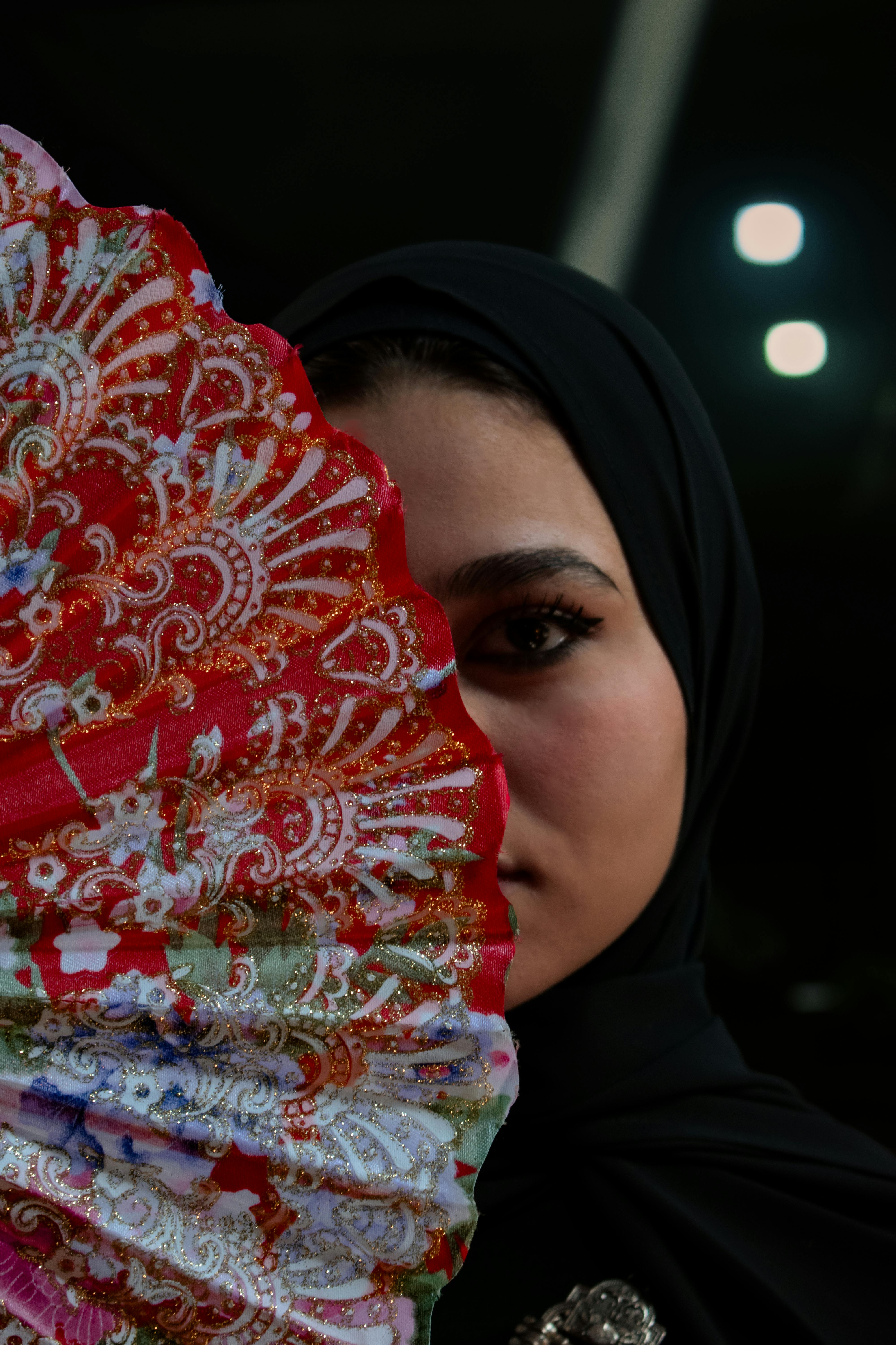 Free Portrait of a woman in hijab holding a colorful fan, conveying elegance and mystery. Stock Photo