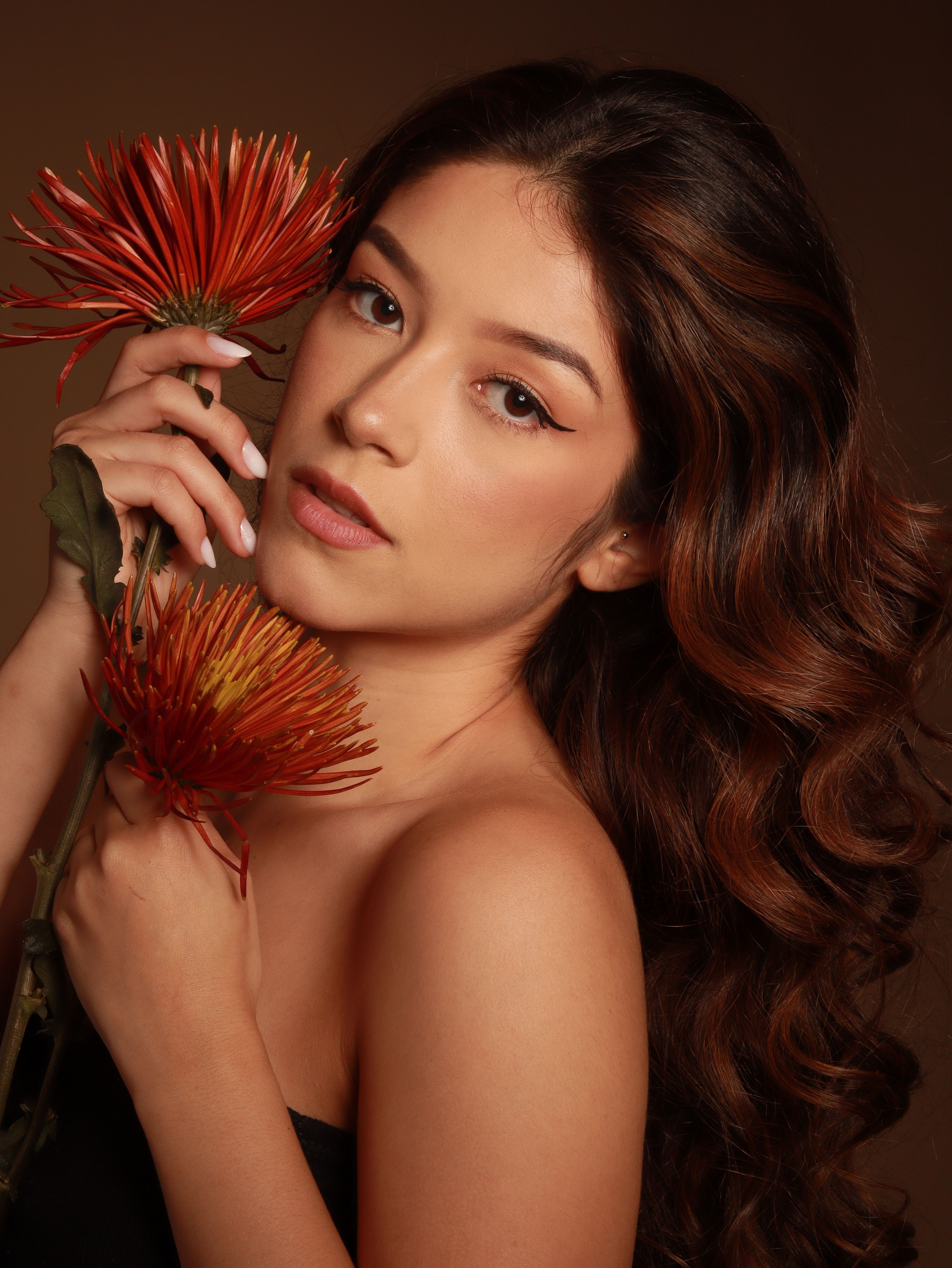 Stunning portrait of a woman with wavy hair holding vibrant flowers against a studio backdrop.
